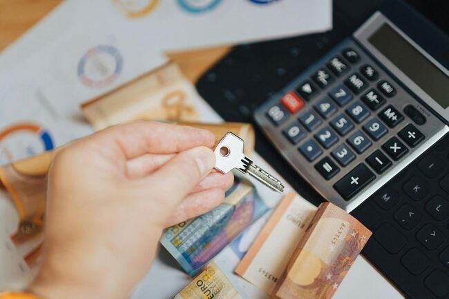 A person holding a key with money and a calculator on a table